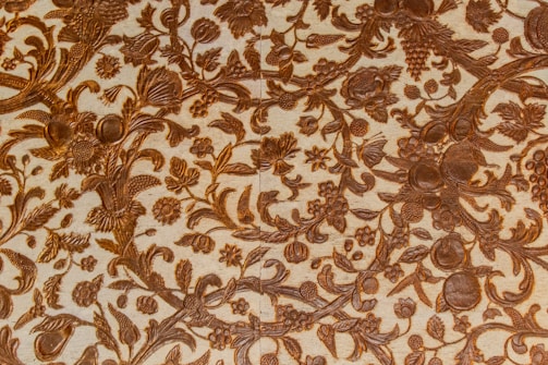 Intricate patterns of floral and foliage designs are carved elegantly into a surface, with detailed depictions of leaves, flowers, and fruits intertwined across the textured background. The craftsmanship reflects a harmonious blend of natural elements creating a vintage or classical aesthetic.