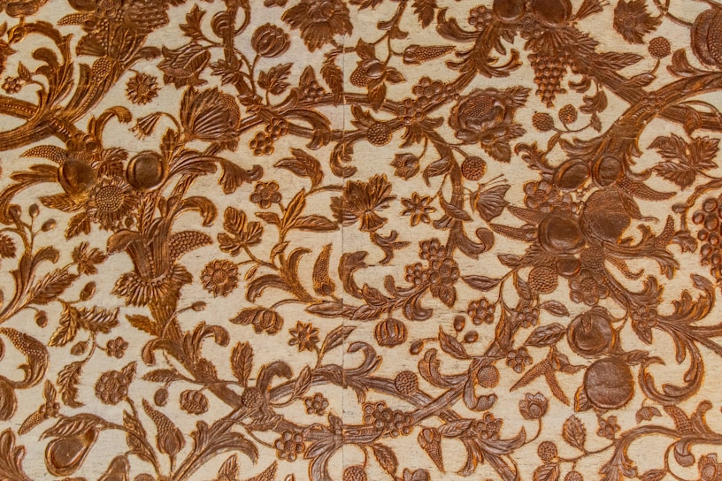 Intricate patterns of floral and foliage designs are carved elegantly into a surface, with detailed depictions of leaves, flowers, and fruits intertwined across the textured background. The craftsmanship reflects a harmonious blend of natural elements creating a vintage or classical aesthetic.