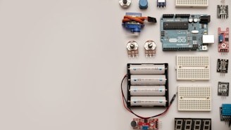 A collection of electronic components including an Arduino board, breadboards, batteries, potentiometers, and various sensors arranged neatly on a flat surface.