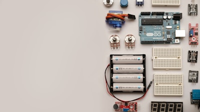 A collection of electronic components including an Arduino board, breadboards, batteries, potentiometers, and various sensors arranged neatly on a flat surface.