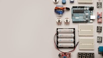 A collection of electronic components including an Arduino board, breadboards, batteries, potentiometers, and various sensors arranged neatly on a flat surface.