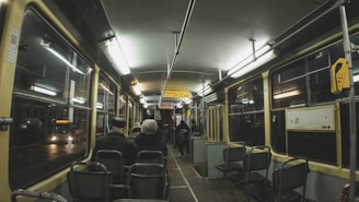 A sleek modern shuttle bus driving through a city street at dusk with warm interior lighting.