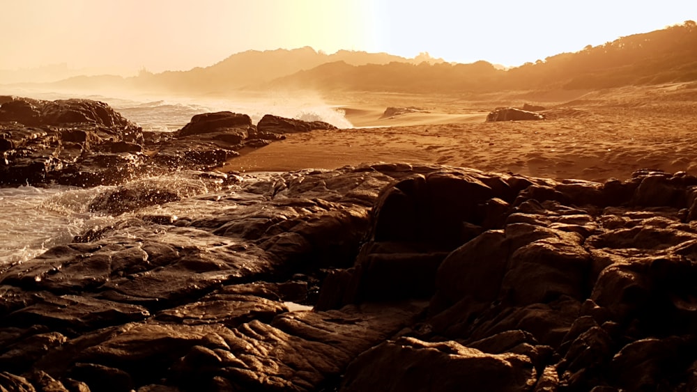 the sun is setting on a rocky beach