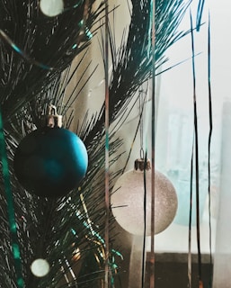 Close-up of colorful Christmas baubles and twinkling fairy lights hanging on a pine branch.