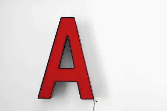 A red, three-dimensional letter 'A' mounted on a plain white background. The shape is bold and the color contrast makes it stand out prominently against the simplicity of the background.