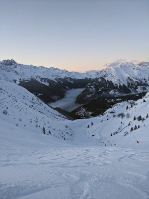 Winter ski slopes and lift lines above a valley village at dusk, with snow-covered ridges beyond