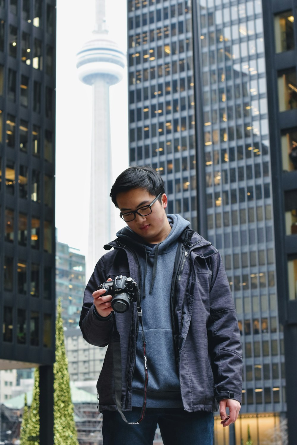 man in gray hoodie holding black DSLR camera outdoors