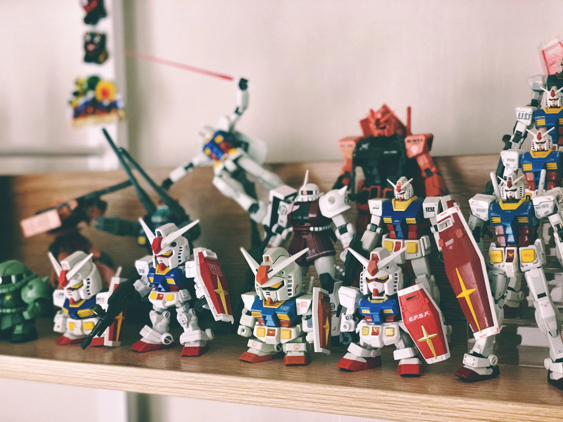 A wooden shelf crowded with small white, blue and red robot models holding red shields