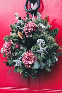 A festive holiday wreath made from handmade fabric flowers in rich reds and greens, hanging on a cozy front door.