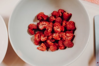 A bowl filled with fresh raspberries alongside a glass of raspberry smoothie on a wooden table.