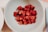 A smiling woman holding a bowl of fresh raspberries in a sunny kitchen.