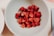 A smiling woman holding a bowl of fresh raspberries in a sunny kitchen.