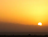 A panoramic view of the sun setting behind the Atlas Mountains, casting golden hues over the rugged peaks.