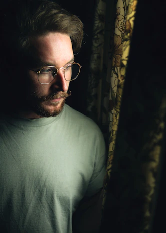 A thoughtful middle-aged man gazing out a window, bathed in soft navy blue light, reflecting quietly.