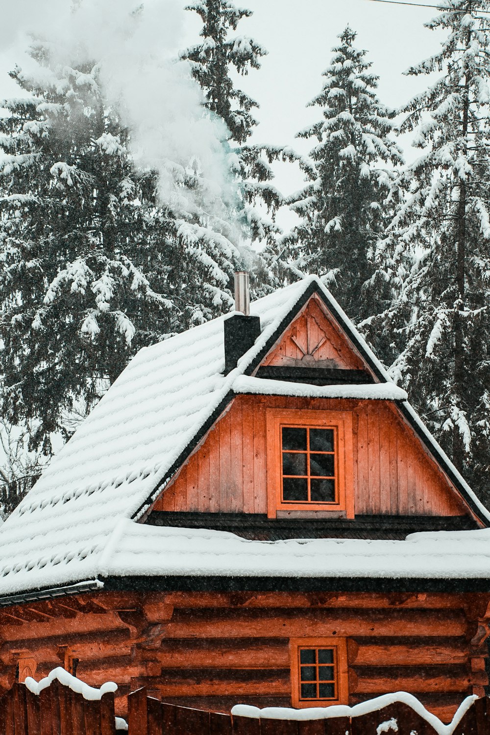 a cabin with snow on the roof and trees in the background