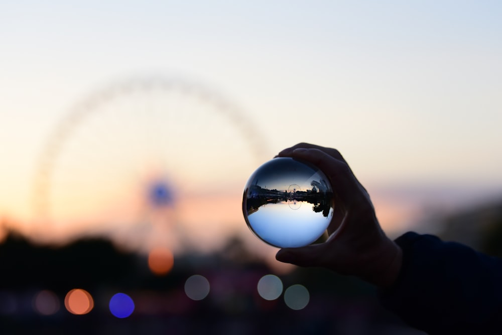 person holding glass ball with reflection of Ferris wheel
