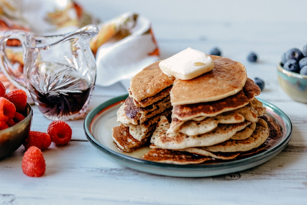 pancakes with butter on top on a round late near raspberry and blueberry fruits