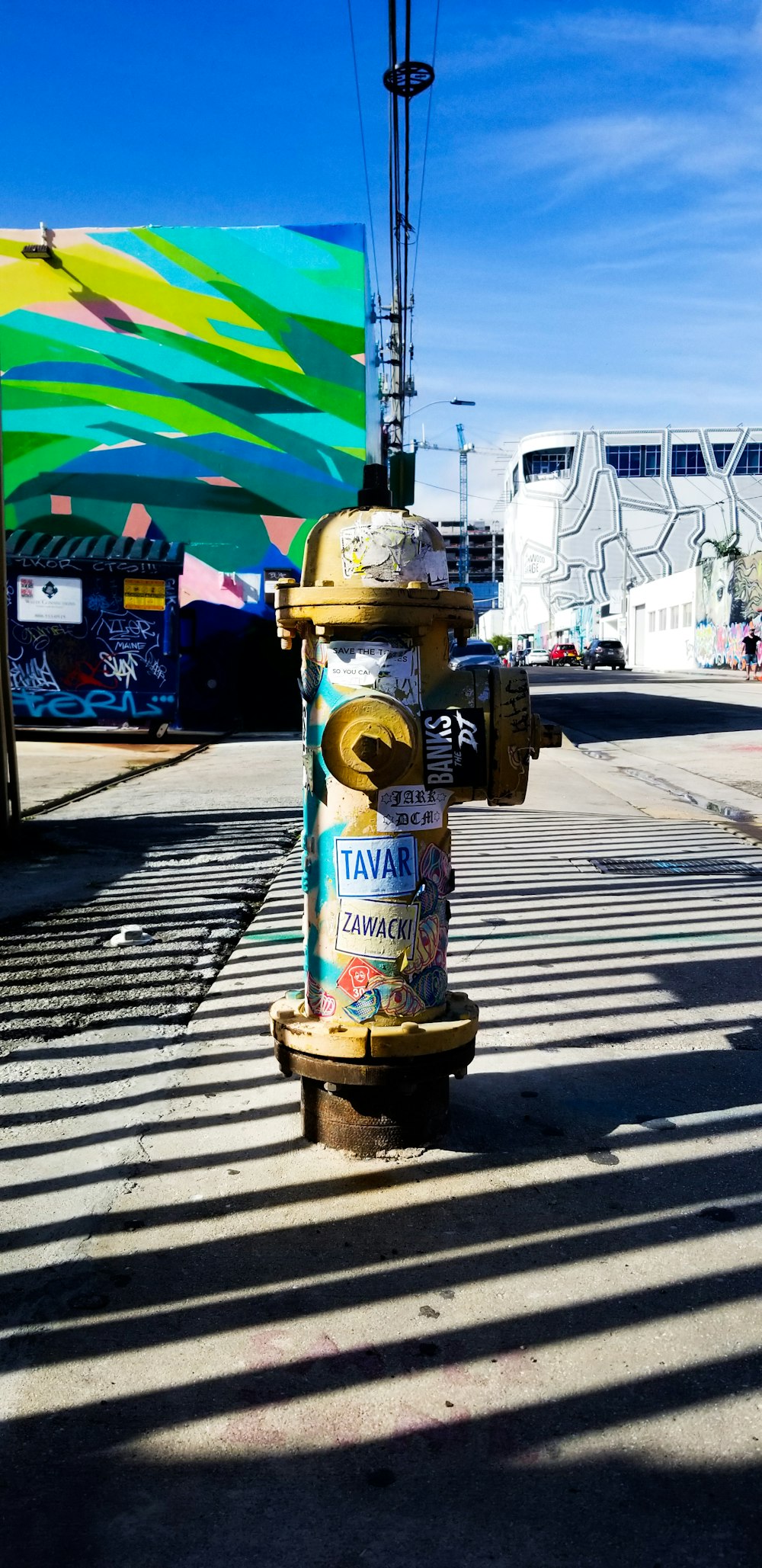 yellow fire hydrant near road viewing building with multicolored art