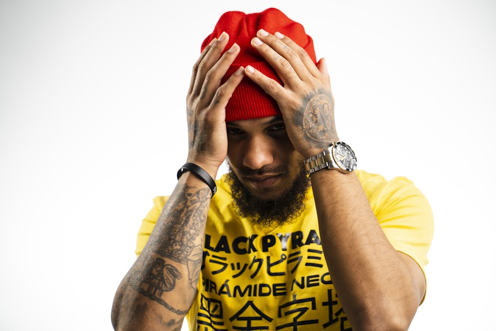 man wearing yellow and black printed crew-neck t-shirt and red knit cap putting both hands on his head