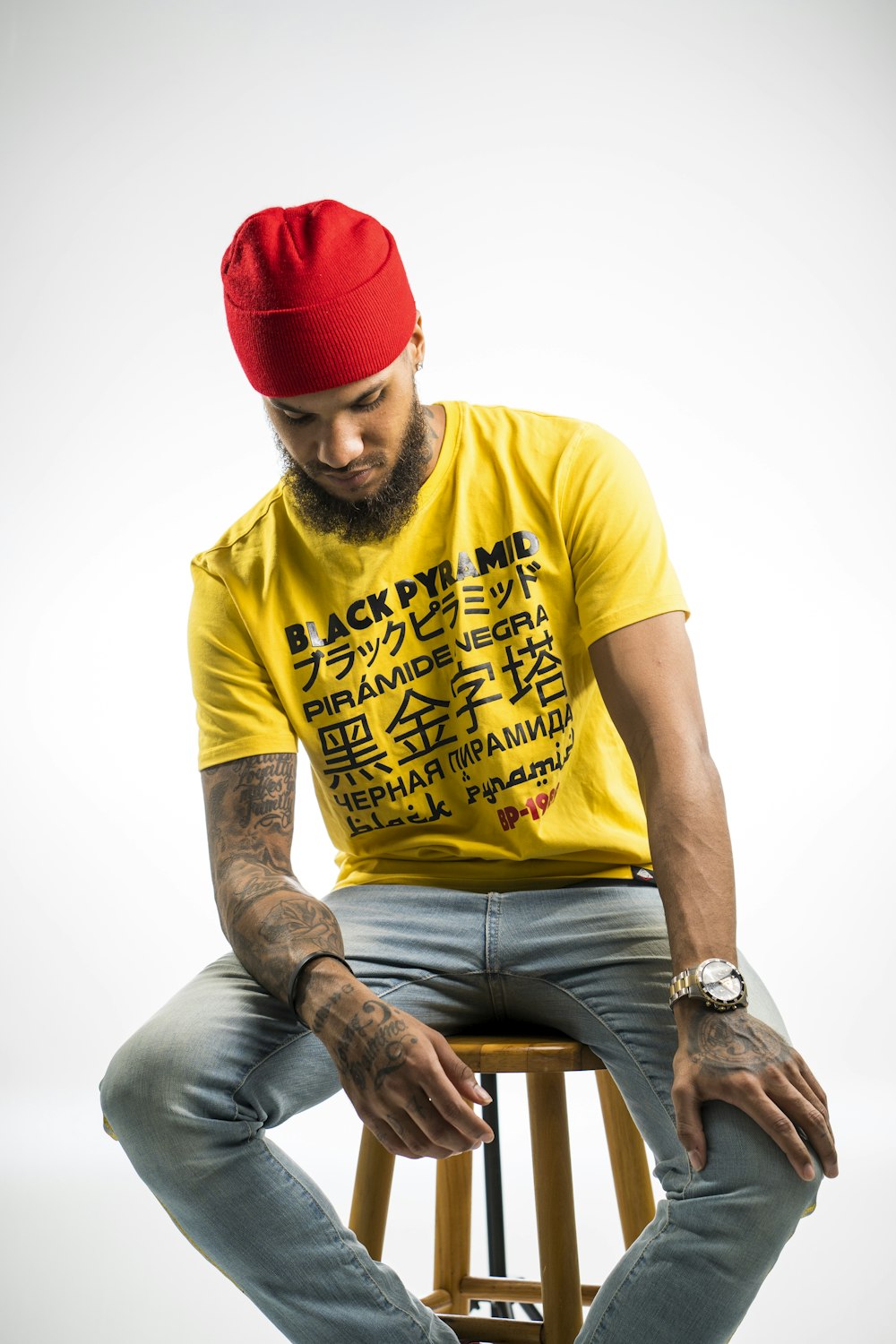 man wearing yellow and black printed crew-neck t-shirt and red knit cap sitting in wooden stool while looking down