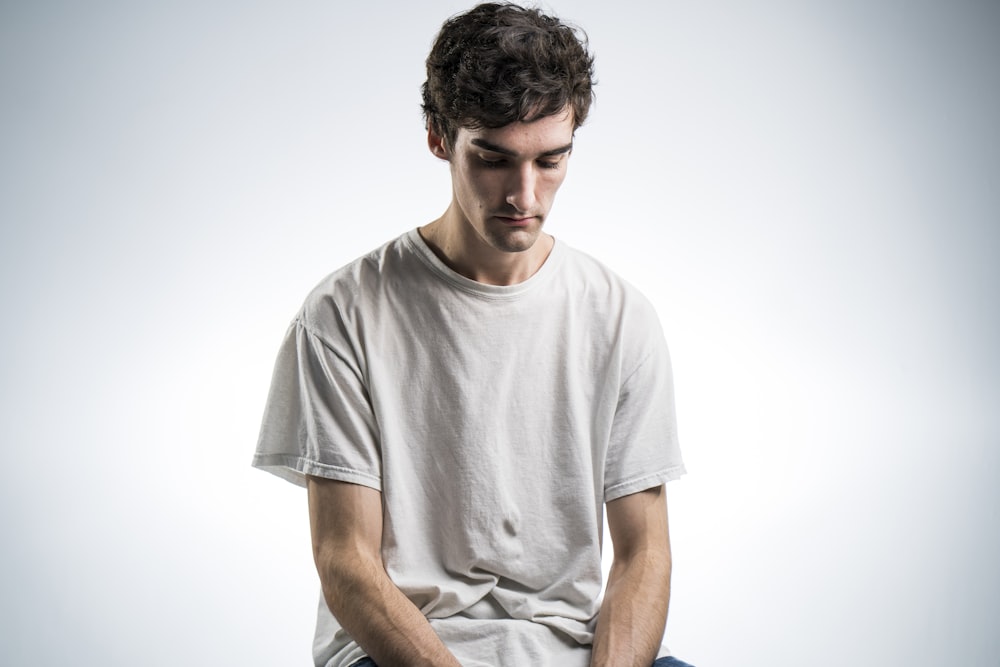 man wearing white crew-neck t-shirt sitting while looking down