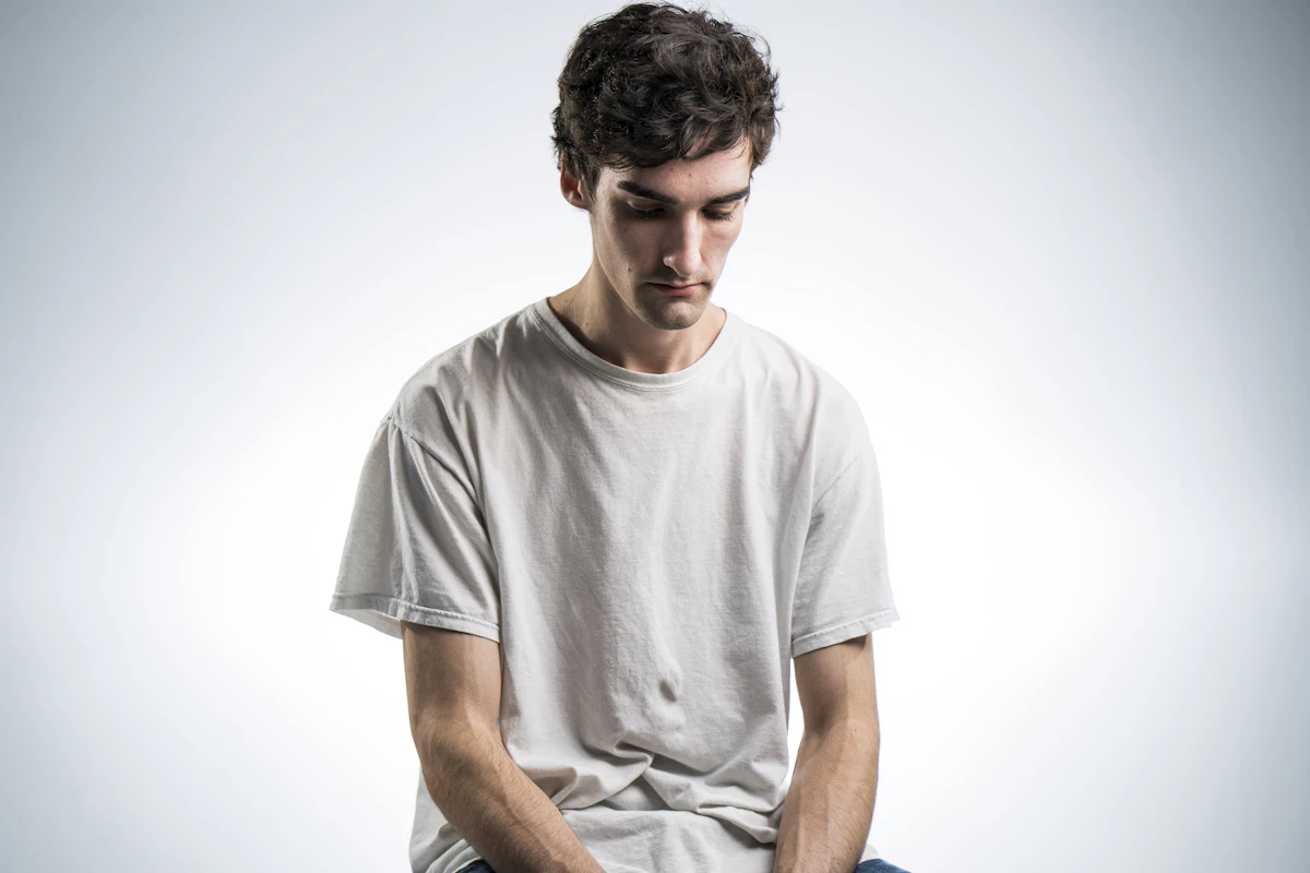 Man sitting and looking down with discomfort, illustrating chronic bloating and digestive issues peptide therapy may help address.