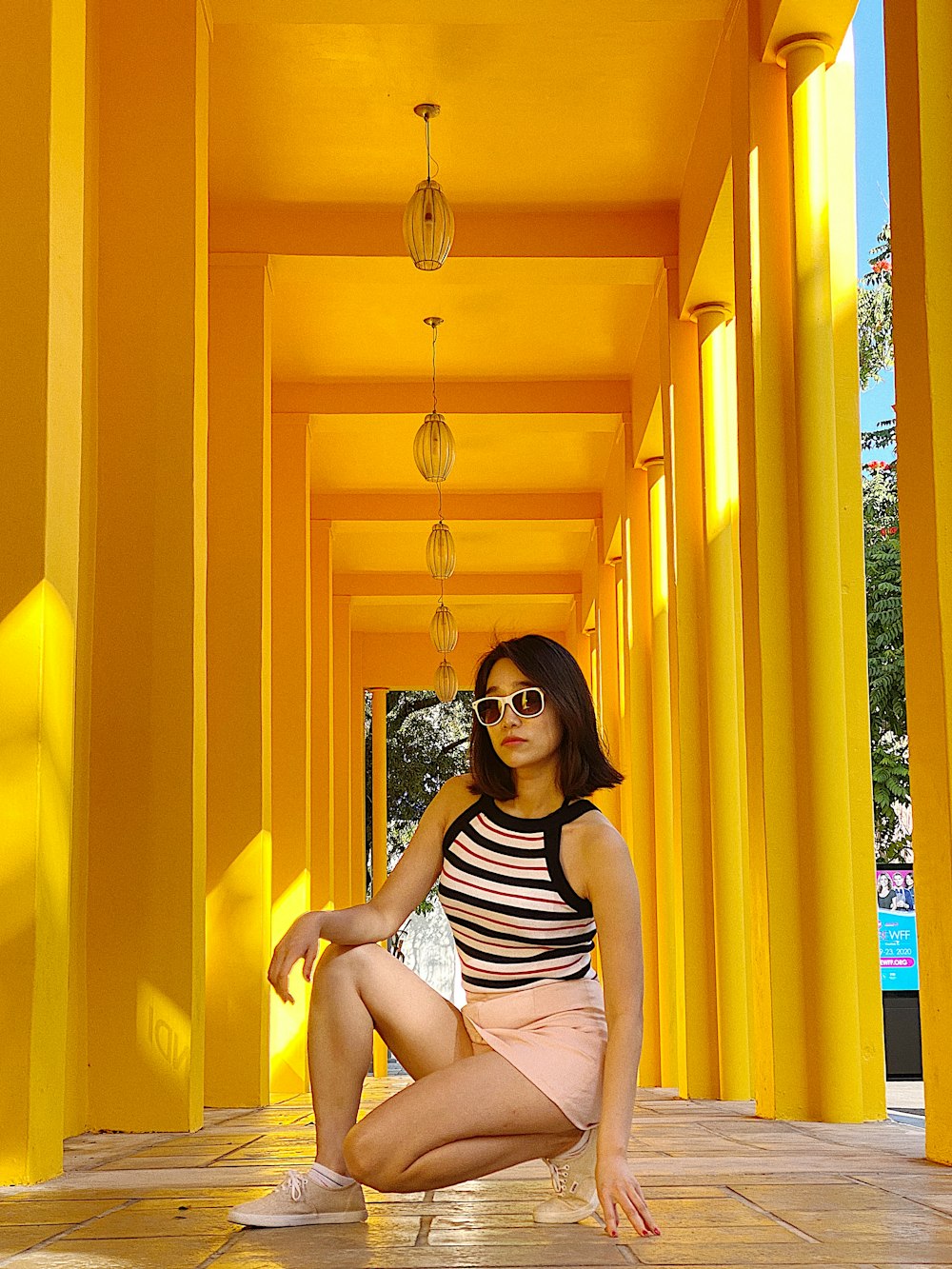 woman wearing black, white, and pink striped spaghetti strap top and sunglasses almost sitting on tiled hallway