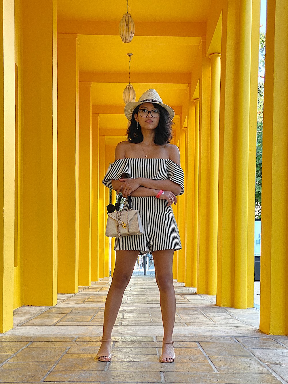 woman wearing black and white striped off-shoulder romper shorts holding white leather handbag standing on tiled hallway