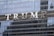 The facade of a tall building is adorned with large, bold letters spelling out a name. The building's exterior is made up of reflective glass panels, which mirror the surrounding environment.