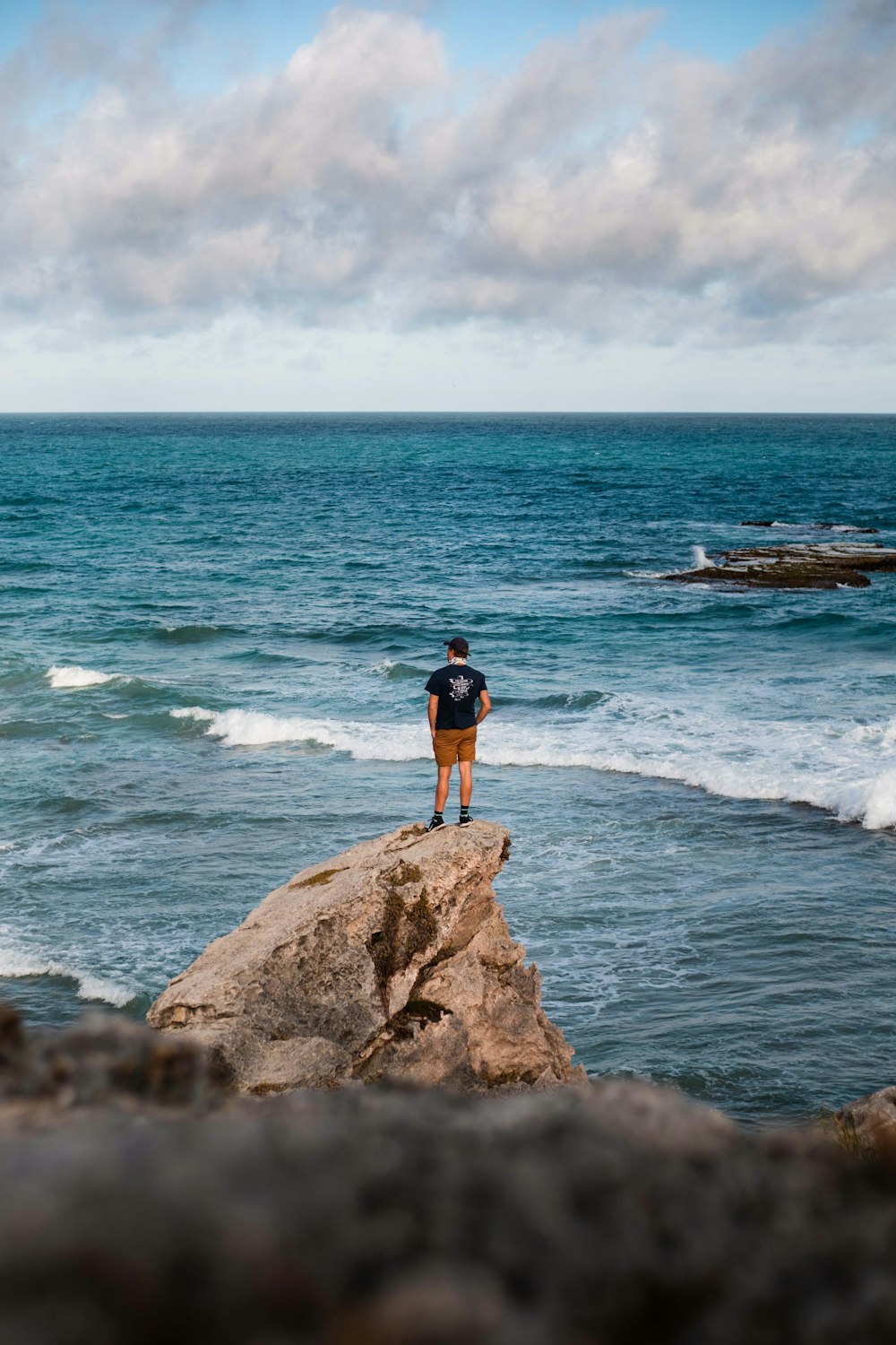 man standing on rock in front of sea during daytime