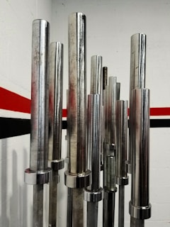Several metallic barbell bars are standing vertically in a room with a red and black stripe running along the white wall.