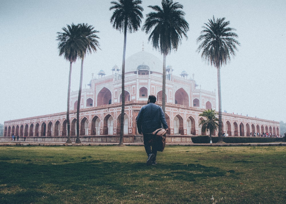 man walking towards temple and trees during day