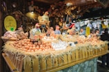 A festive market stall displays a variety of fresh eggs piled on straw, surrounded by decorative ceramic chickens. The wooden stall is adorned with rustic decorations, creating a quaint village market atmosphere.