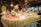 A festive market stall displays a variety of fresh eggs piled on straw, surrounded by decorative ceramic chickens. The wooden stall is adorned with rustic decorations, creating a quaint village market atmosphere.