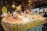 A festive market stall displays a variety of fresh eggs piled on straw, surrounded by decorative ceramic chickens. The wooden stall is adorned with rustic decorations, creating a quaint village market atmosphere.