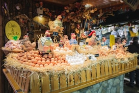 A festive market stall displays a variety of fresh eggs piled on straw, surrounded by decorative ceramic chickens. The wooden stall is adorned with rustic decorations, creating a quaint village market atmosphere.