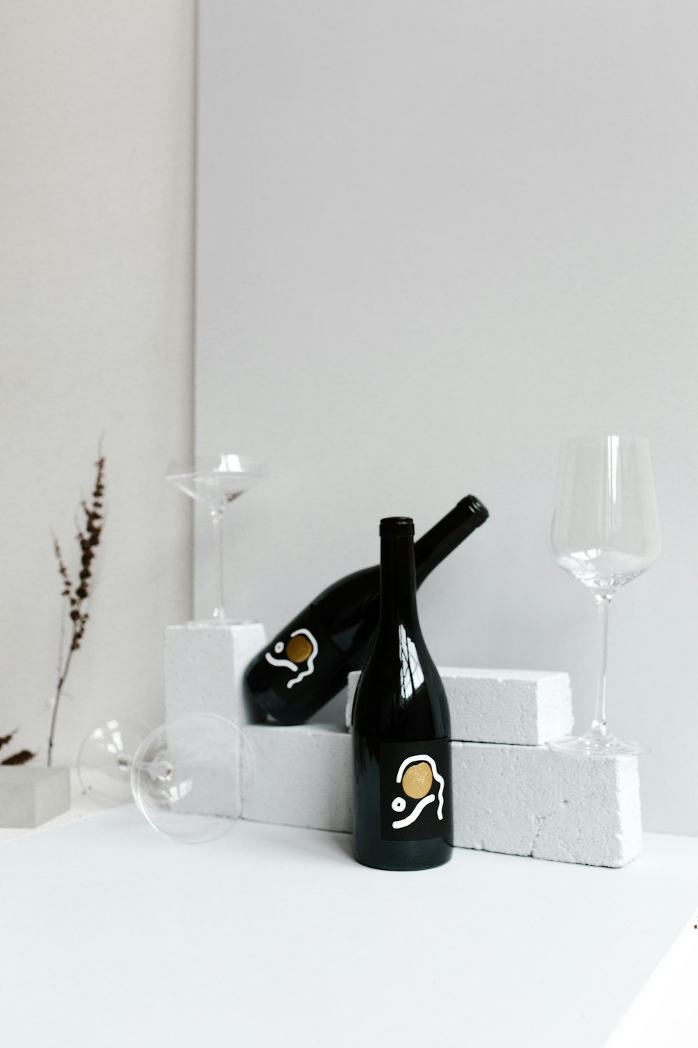 due bottiglie di vino nere e tre bicchieri da vino su superficie bianca