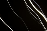 Abstract dynamic light artwork with flowing lines of soft white and gray hues on black background.