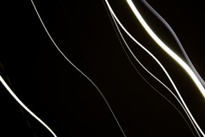 Abstract dynamic light artwork with flowing lines of soft white and gray hues on black background.