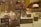A display case filled with various types of jewelry including ornate earrings, rings, and bracelets, all set on beige display stands. The background features blurred images of floral designs and metallic patterns, contributing to an elegant and opulent atmosphere.