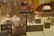 A display case filled with various types of jewelry including ornate earrings, rings, and bracelets, all set on beige display stands. The background features blurred images of floral designs and metallic patterns, contributing to an elegant and opulent atmosphere.