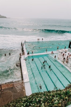 photography of people gathering near swimming pool beside seashore during daytime