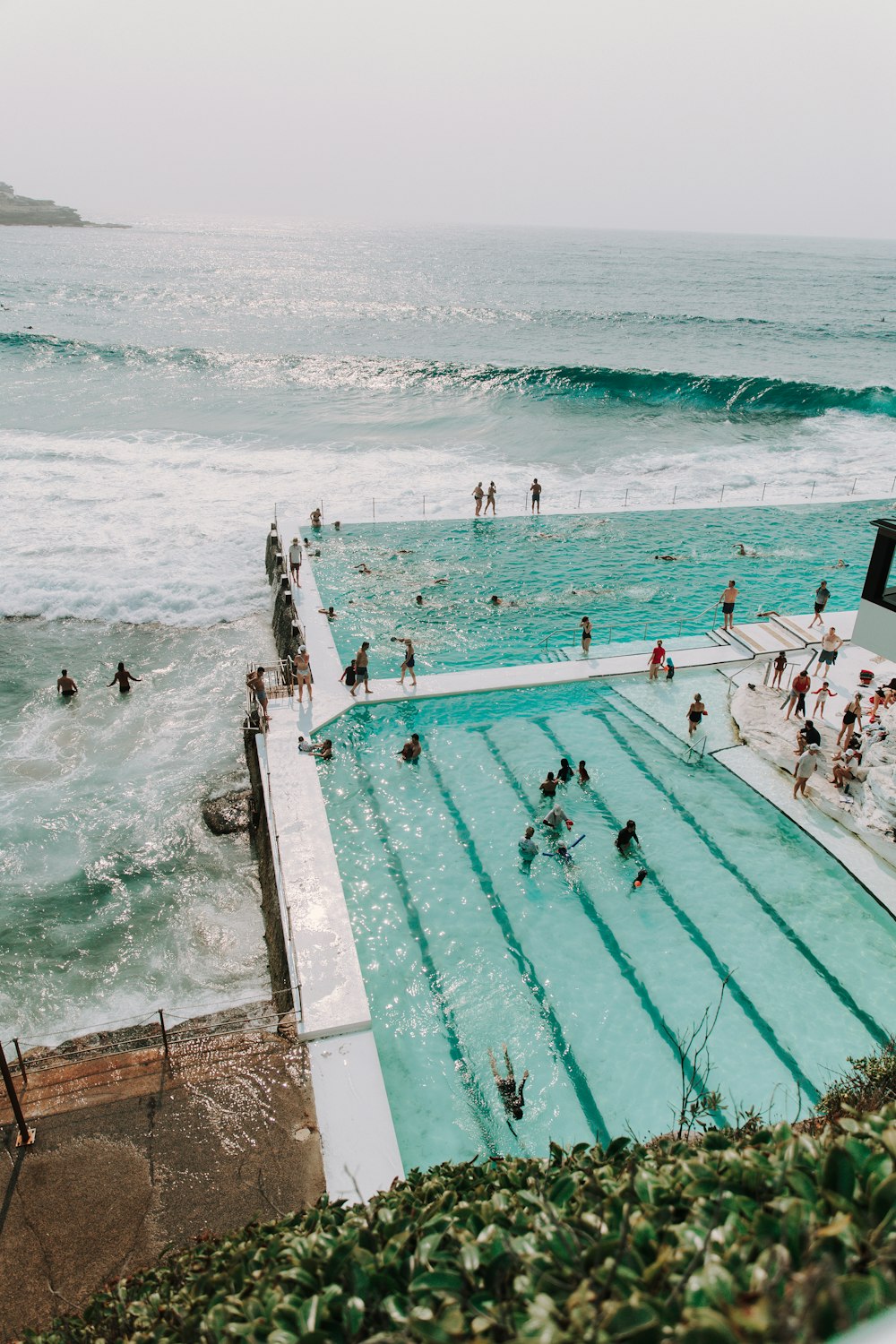 Fotografie von Menschen, die sich tagsüber in der Nähe des Swimmingpools am Meer versammeln