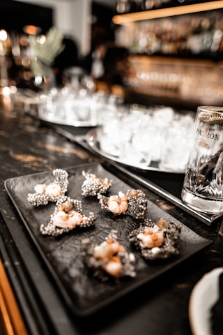 Close-up of a plate with a variety of appetizing bar snacks and drinks on a dark wooden table.