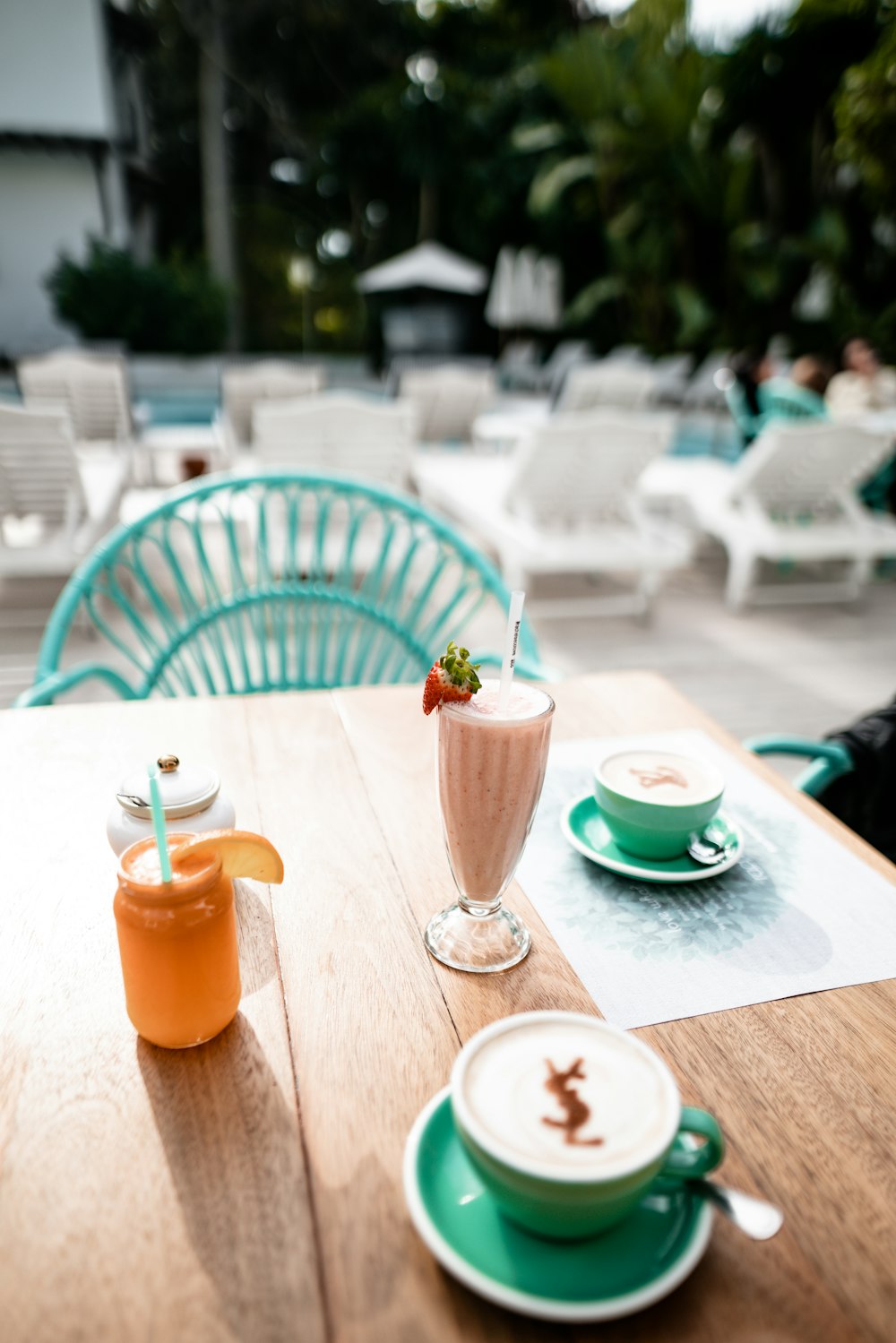 green ceramic coffee cup with cappuccino beside smoothies and orange juice on table