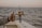 A boat fishing trip on the open sea with a fishing reel mounted on the side of the boat. The ocean stretches to the horizon under a clear sky, and a person gives a thumbs-up gesture, indicating approval or success.