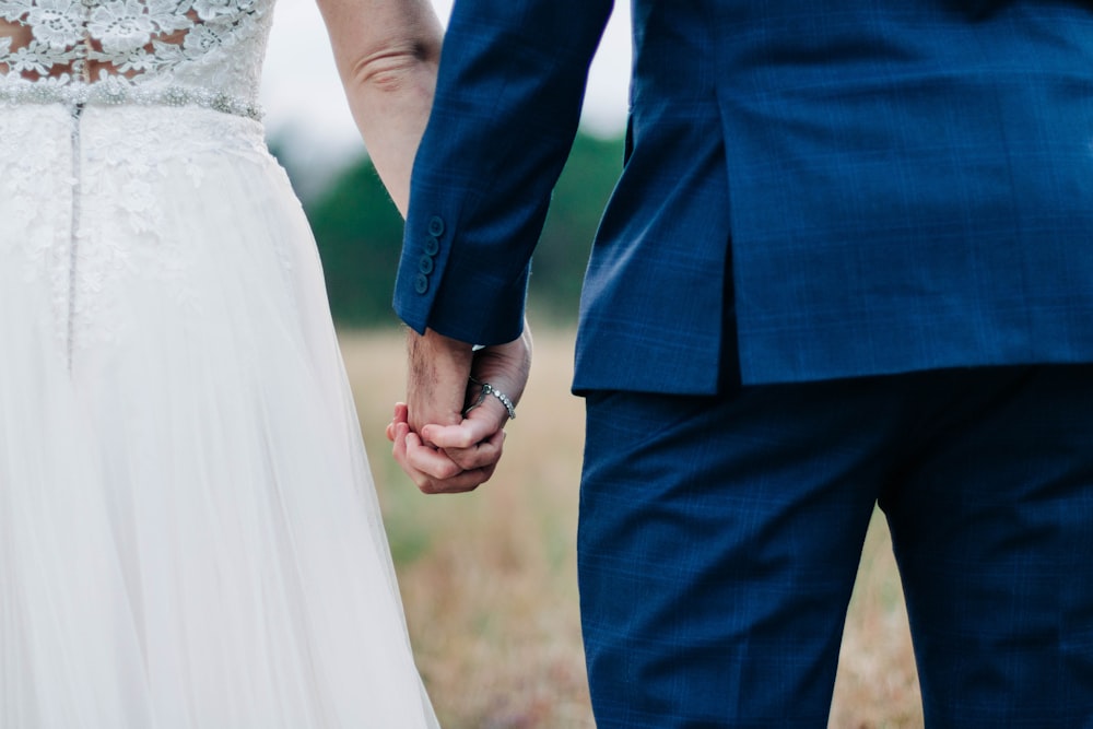woman wearing white wedding dress and man wearing blue suit holding hands during daytime