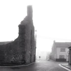 A serene black-and-white image of an ancient European street drenched in soft morning fog