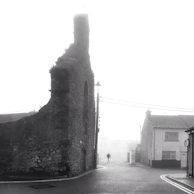 A serene black-and-white image of an ancient European street drenched in soft morning fog