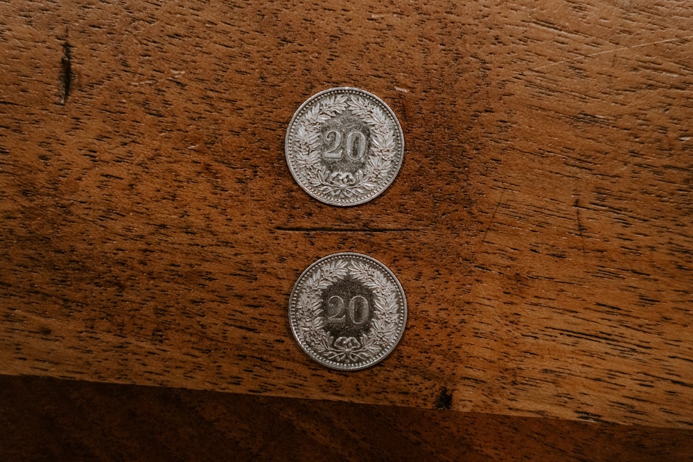 two round silver-colored 20 coins on brown surface
